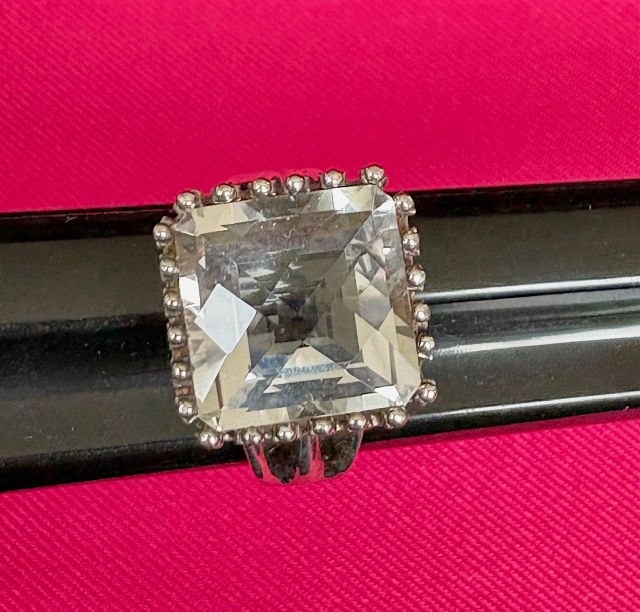 Ring with a large square gemstone on a pink background