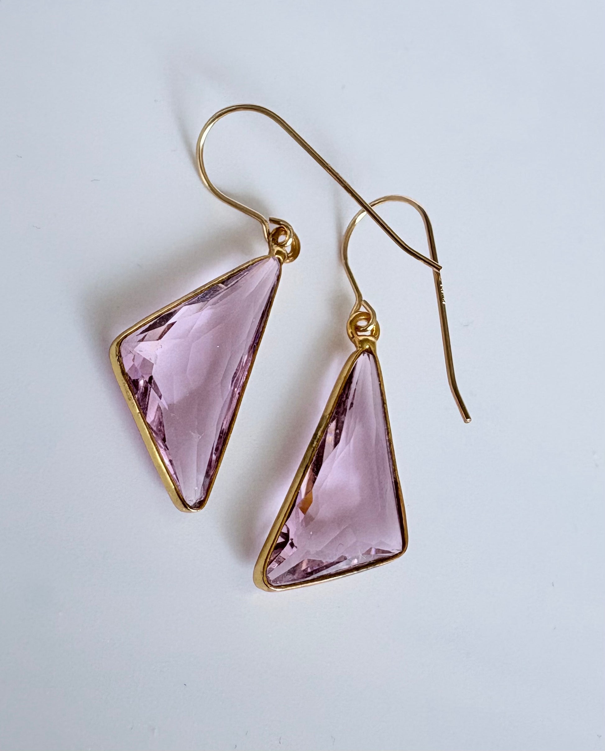 Gold earrings with pink triangular gemstones on a light gray background