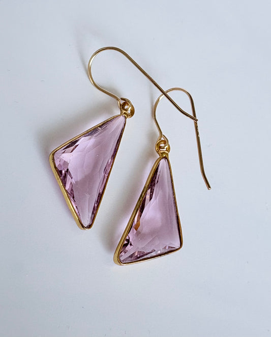 Gold earrings with pink triangular gemstones on a light gray background