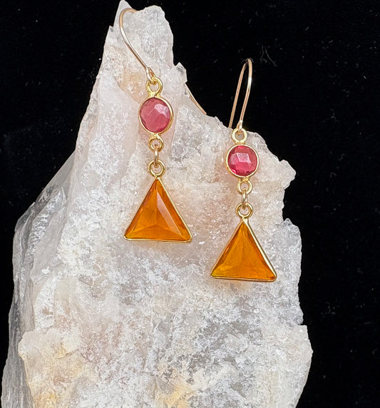 Gold earrings with orange and pink gemstones on a crystal background