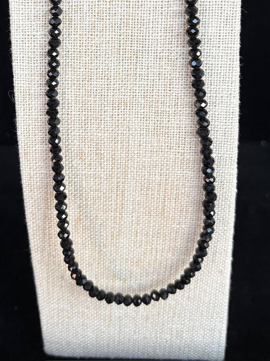 Black gemstone beaded necklace on a white fabric background