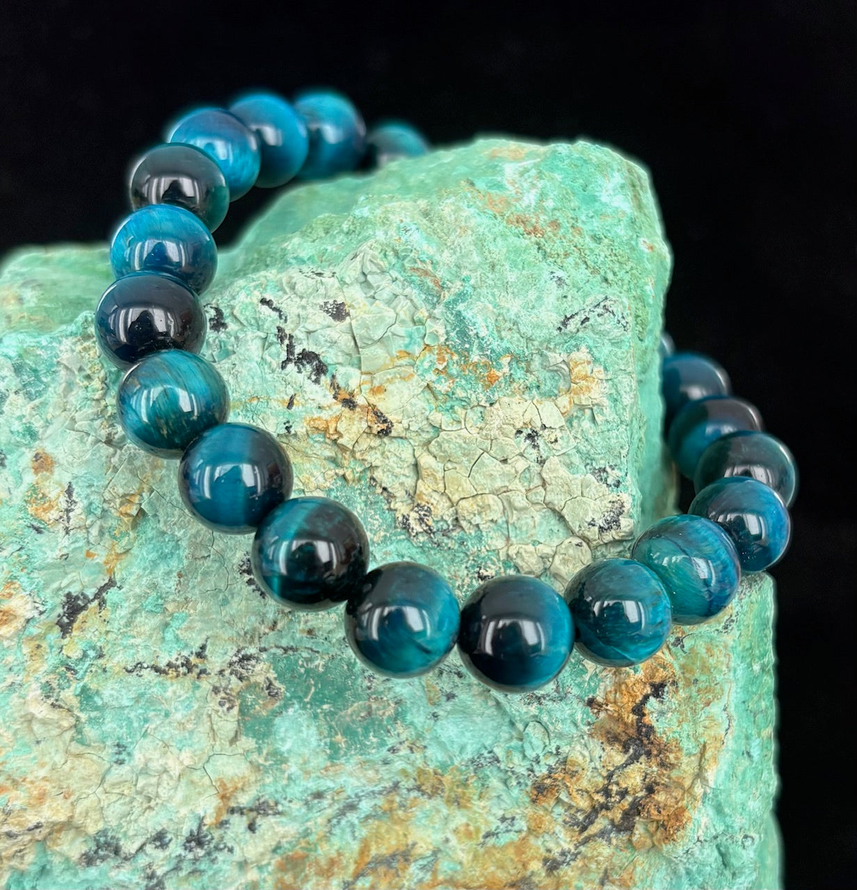 Blue Tiger's Eye beaded bracelet on a green stone with a black background