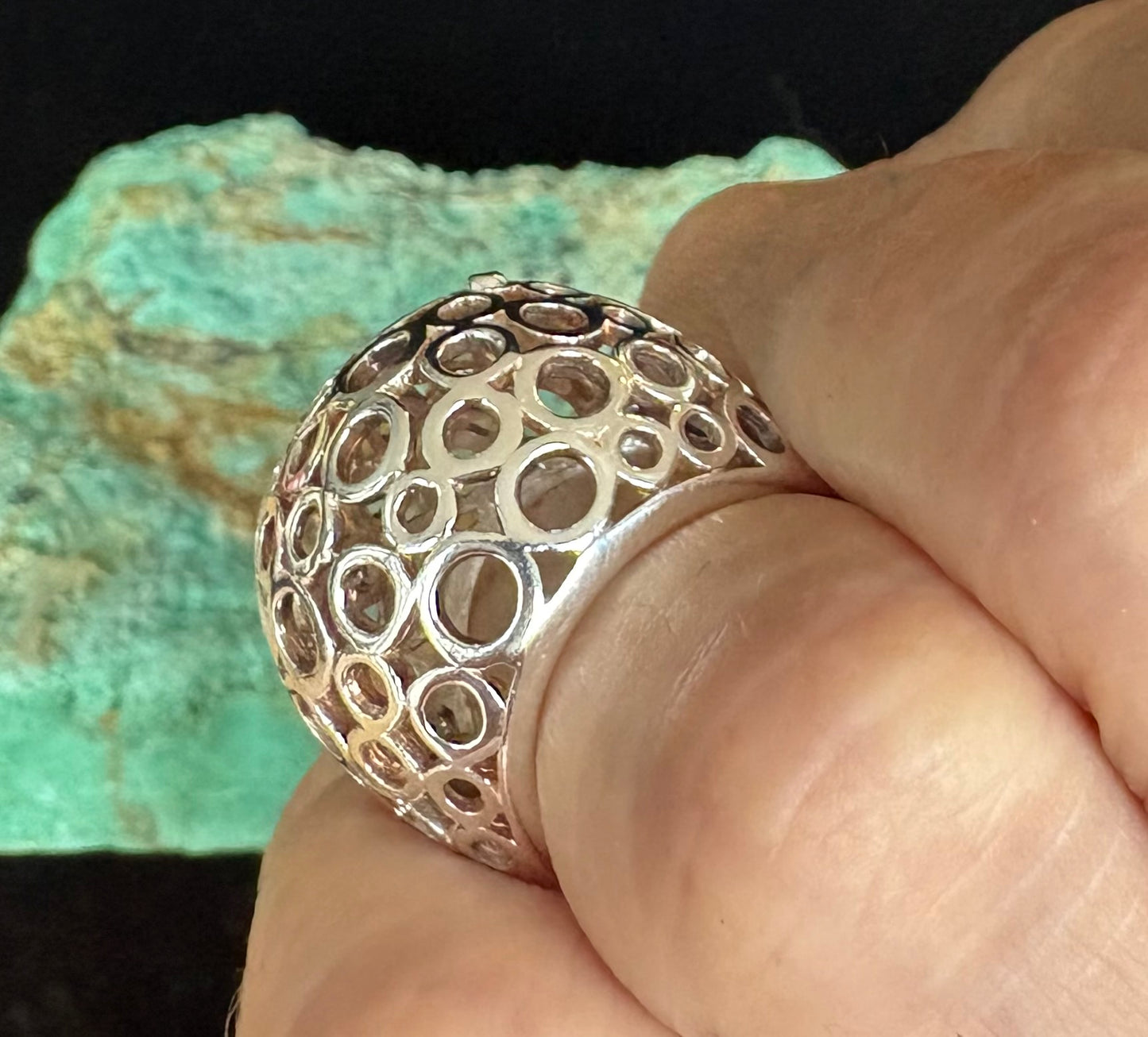 Silver ring with intricate design held by a hand against a textured green background