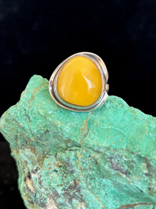 Silver ring with a yellow amber stone on a green rock against a black background