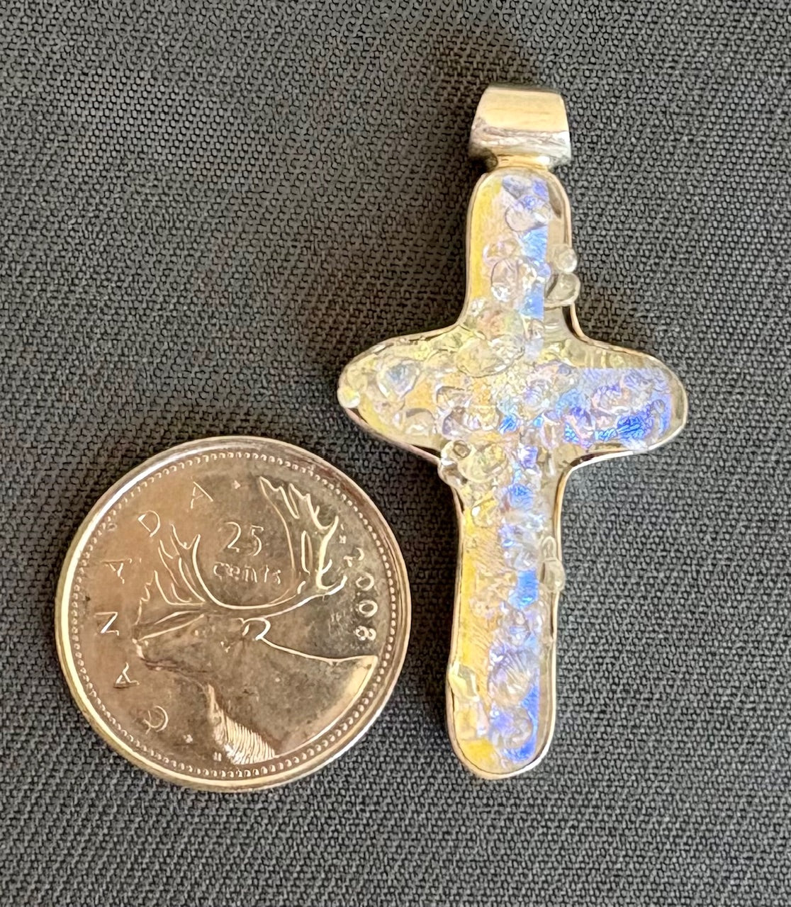 Dichroic glass cross pendant next to a New Zealand 25 cent coin on a gray background