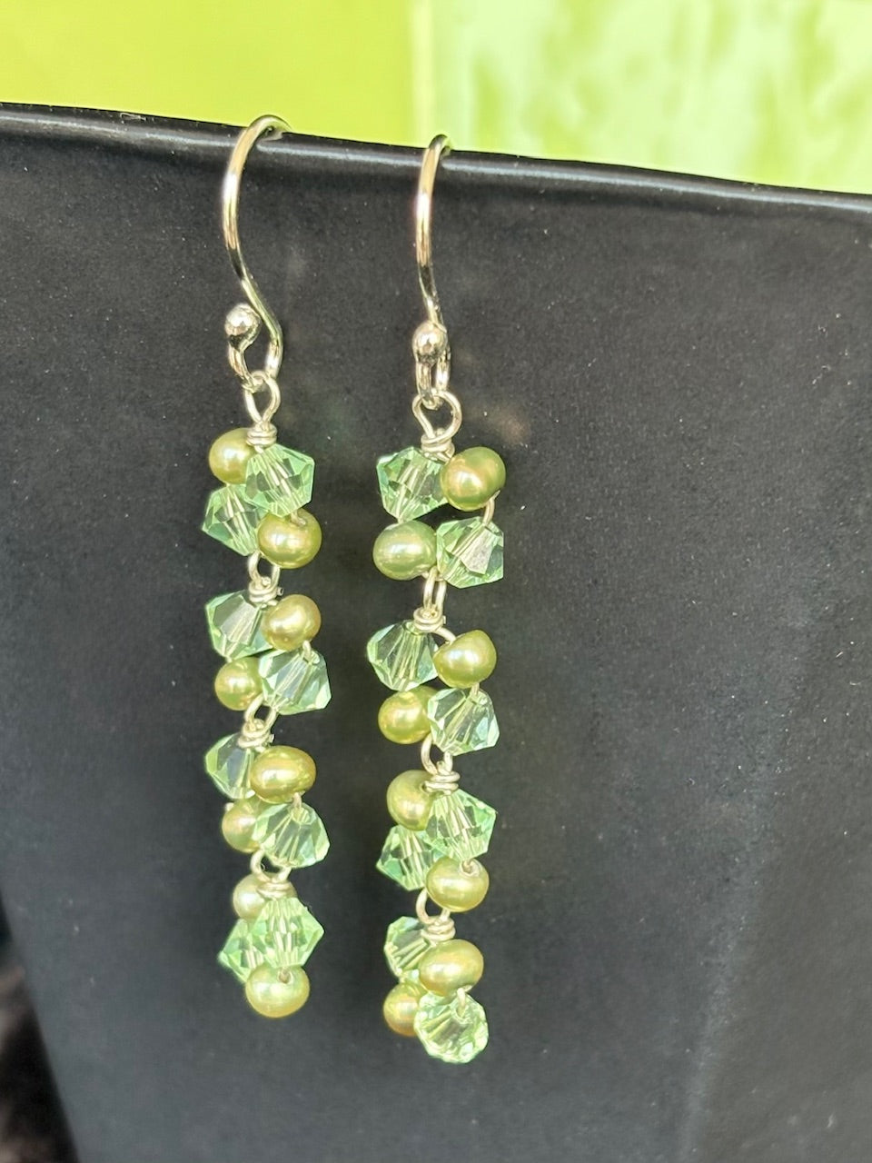Green beaded earrings on a dark surface with a green background