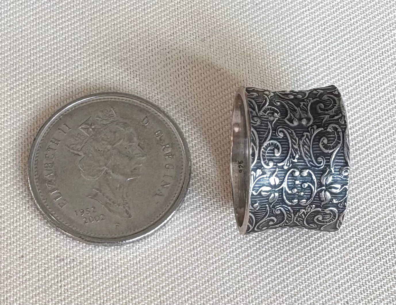 Silver ring with intricate design next to a coin on a textured fabric background
