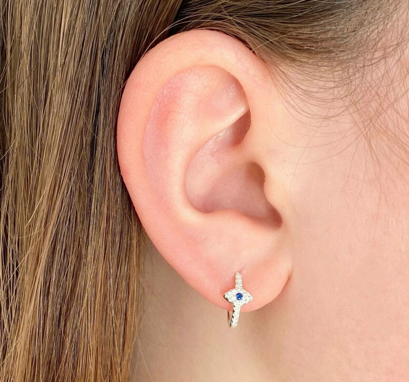 Close-up of an ear wearing a small silver earring with a blue gemstone.