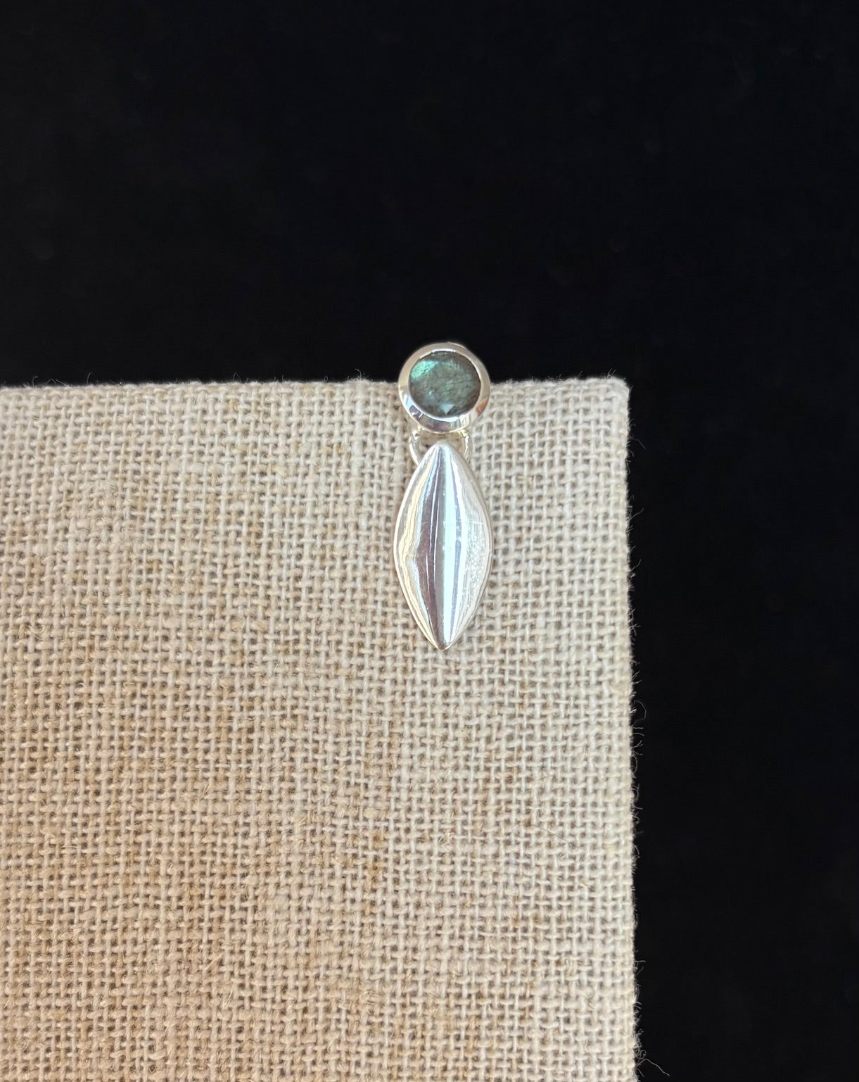 Silver earring with a labradorite gemstone on a beige fabric background