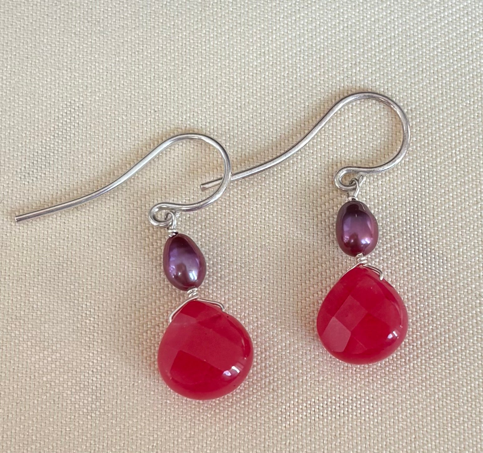 Pair of earrings with fuchsia teardrop gemstones and purple pearls on a beige background