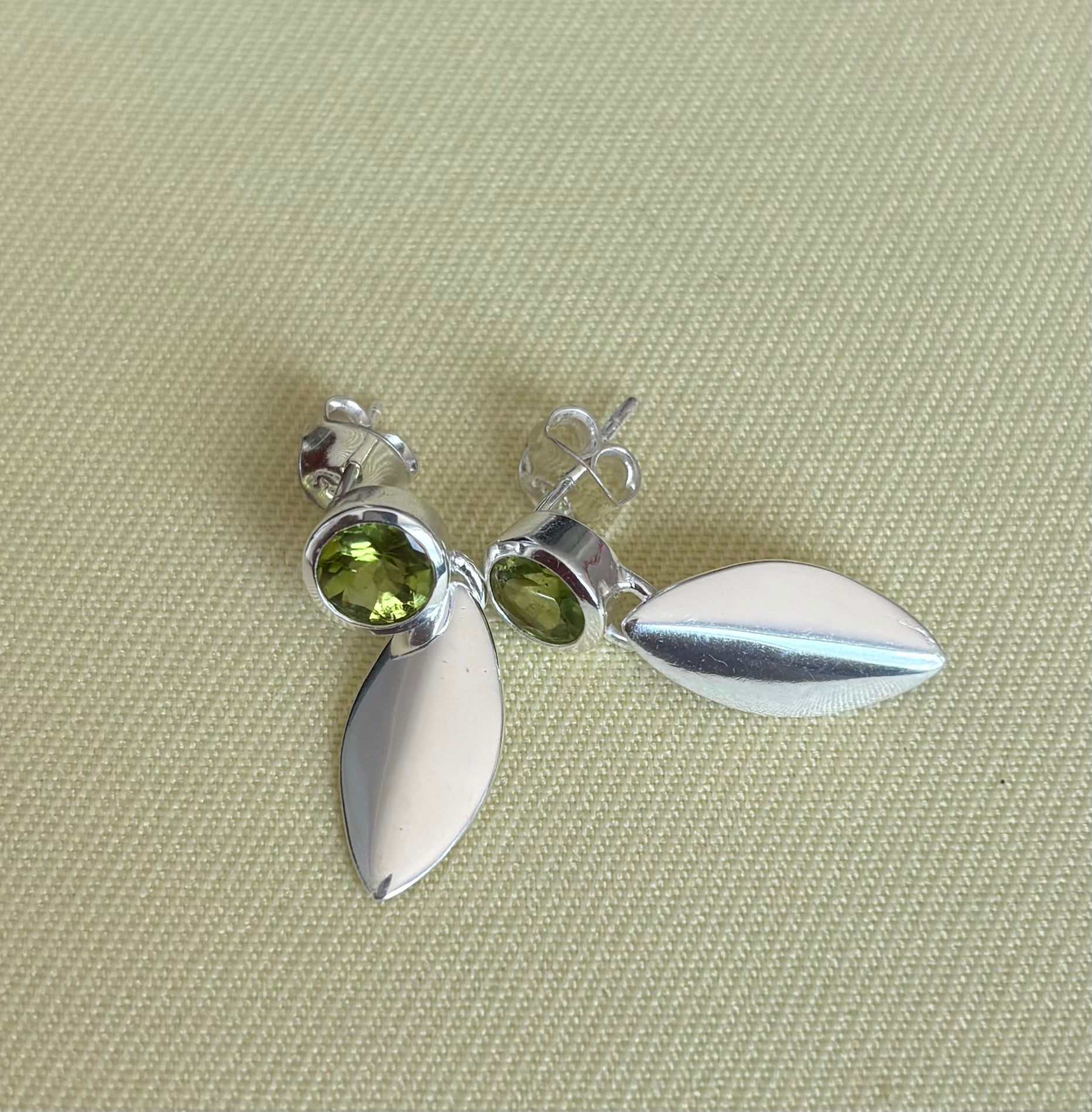 Silver earrings with green gemstones on a textured beige surface