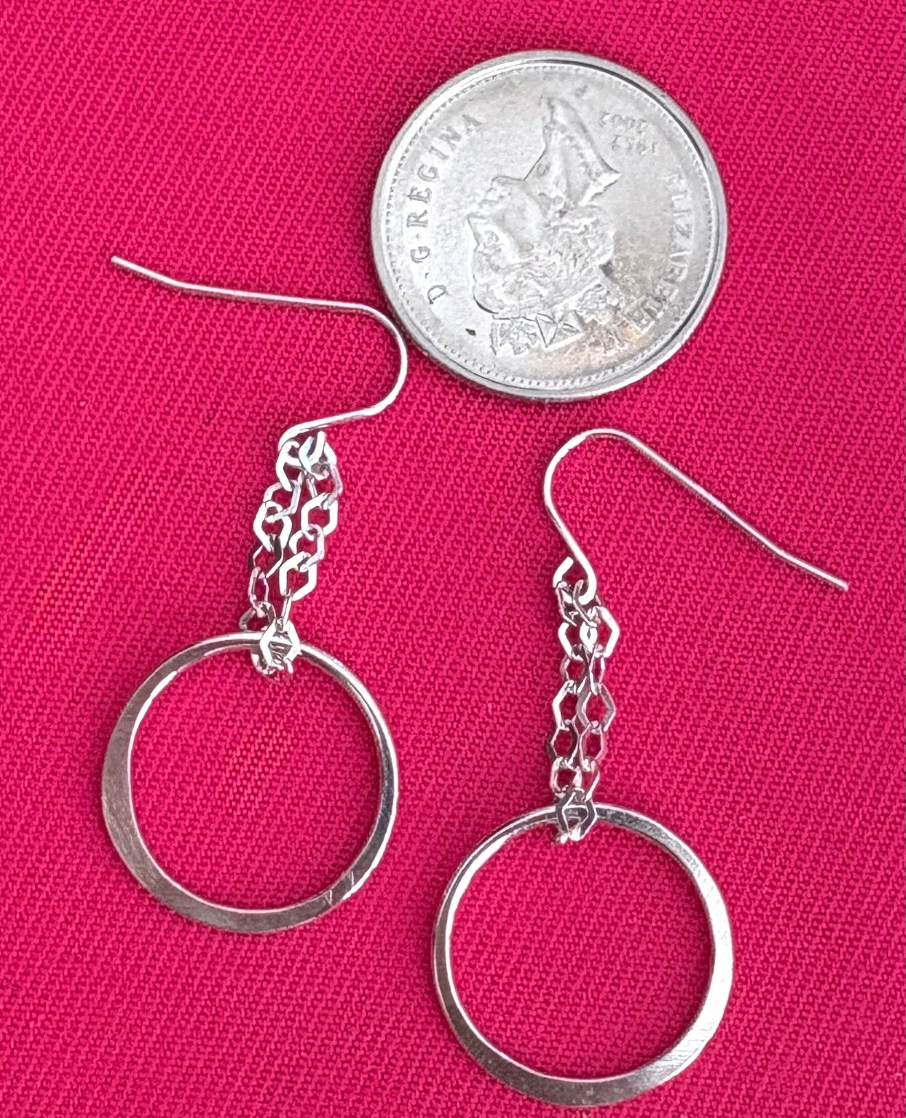 Silver hoop earrings on a pink background with a quarter for scale.
