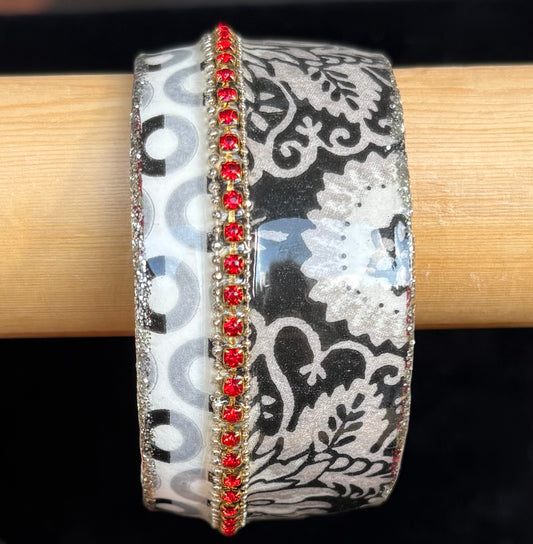 Decorative bangle with floral pattern and red stones on a wooden stick. Made by Iris Design