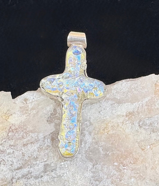 Cross-shaped pendant with opal-like inclusions on a dark background