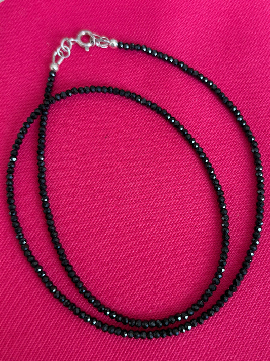 Black micro faceted spinel necklace on a pink background