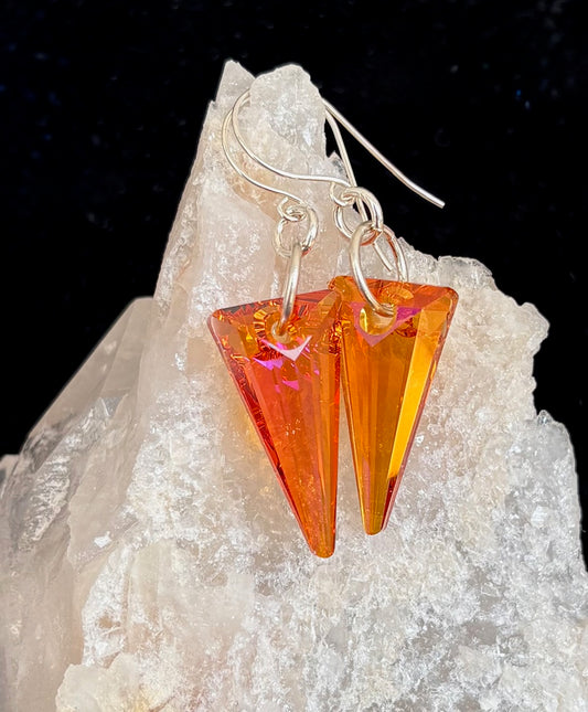 Orange triangular earrings on a rock with a dark background