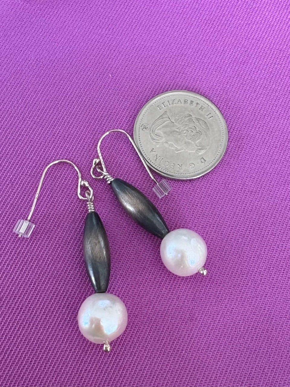 Pair of earrings with Navajo Silver and Pearls on purple background with a coin for scale.