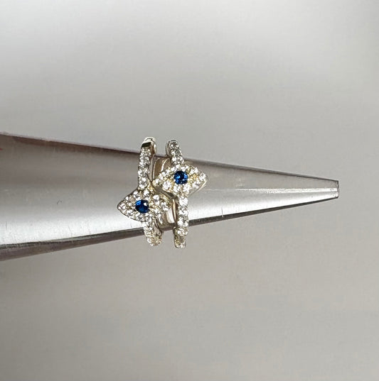 Evil eye earrings with blue gemstones on a metallic surface by Jolie Esprit