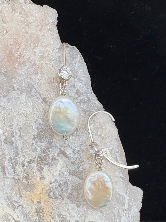 Pearl earrings with silver hooks on a rock and black background