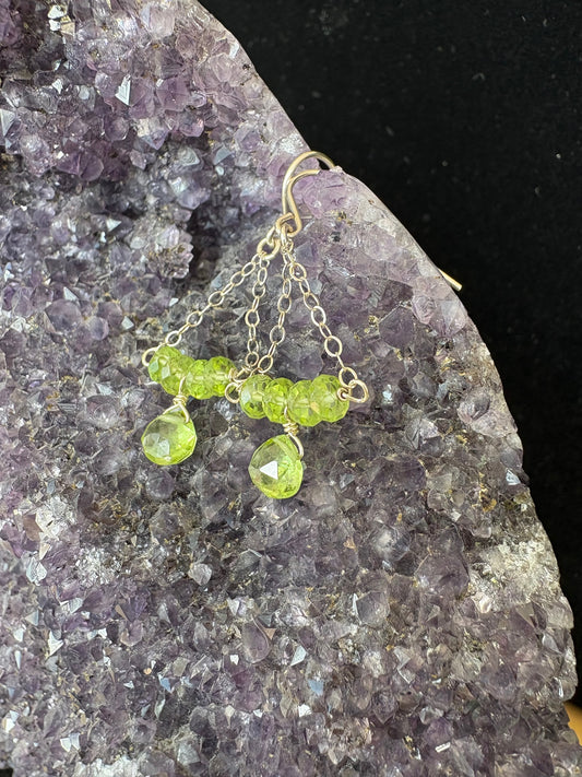 Green peridot gemstone beaded earrings on a dark stone surface 