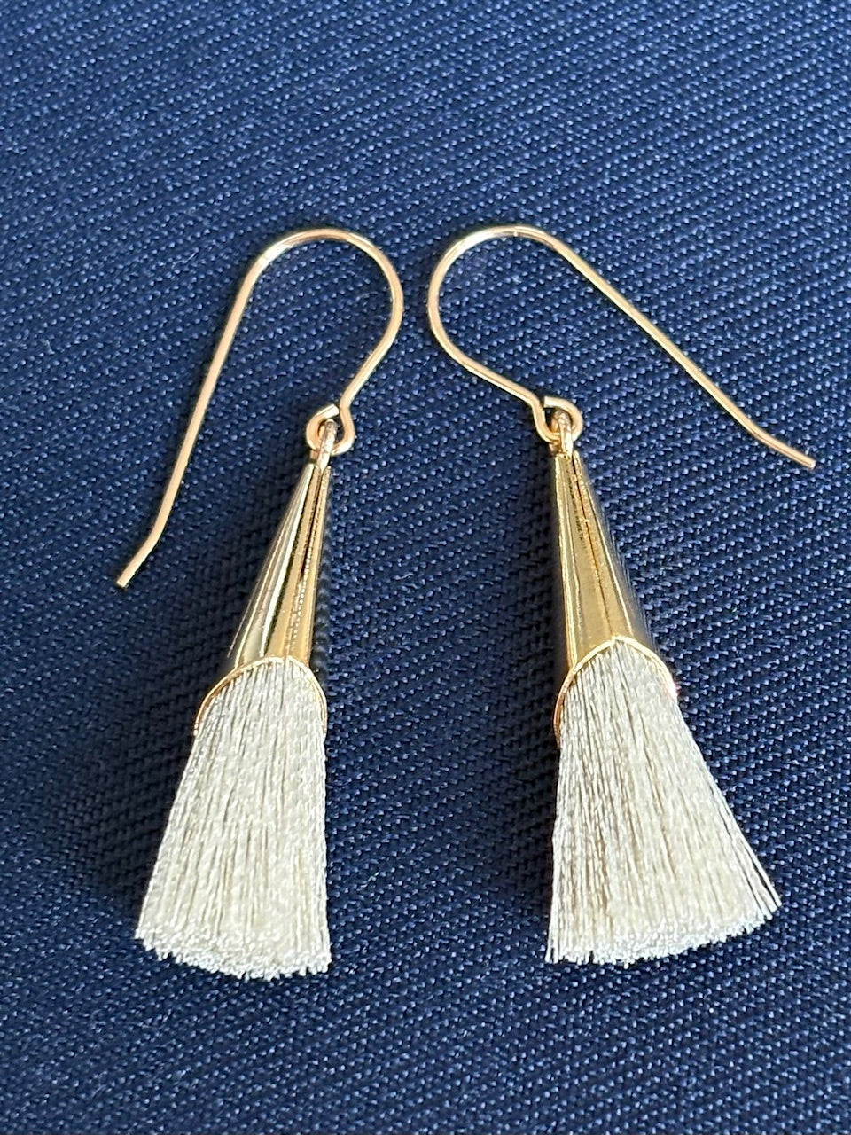 Gold and silver tassel earrings on a blue textured background