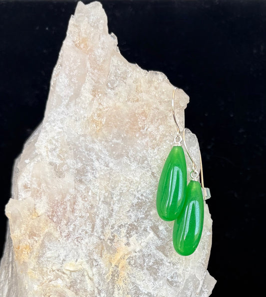 Green teardrop gemstone earrings on a rock with a dark background