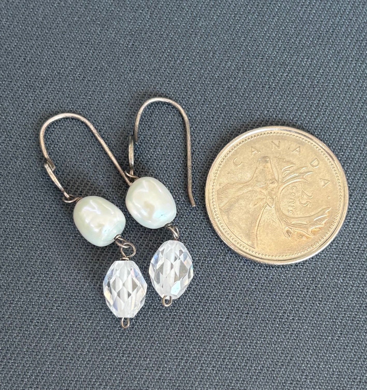 Pair of earrings with pearls and clear crystals next to a coin on a gray background