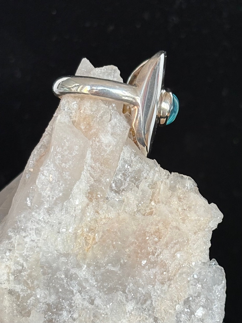 Silver ring with a  blue topaz gemsstone on a crystal rock against a dark background 