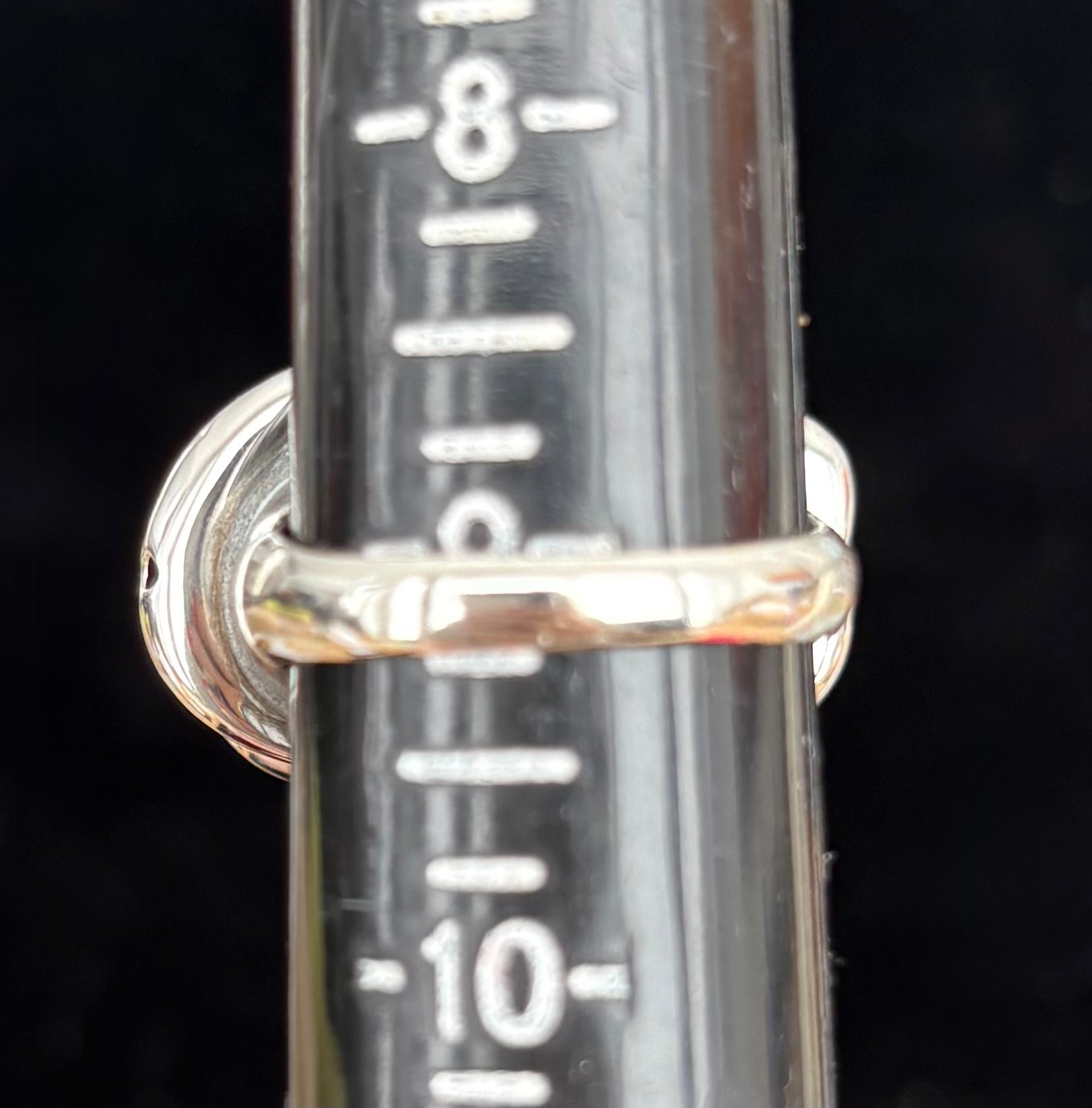 Silver ring with a cylindrical metal component featuring measurement markings on a black background