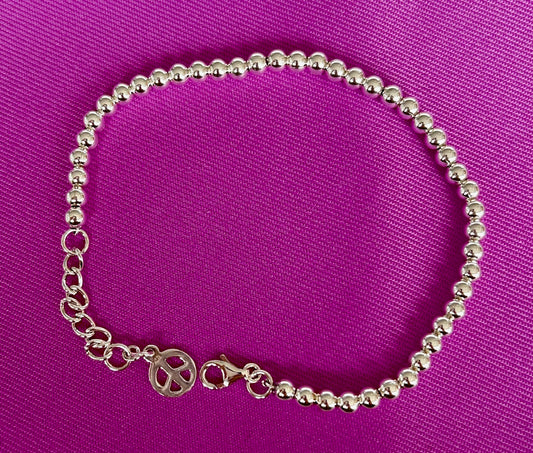Jolie Esprit Sterling Silver beaded ball bracelet with a peace sign charm on a purple background