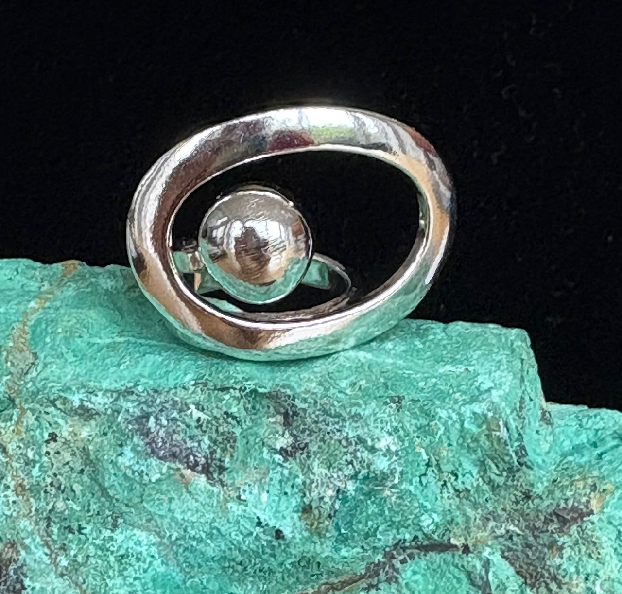 Silver ring with an offset orb  green stone background