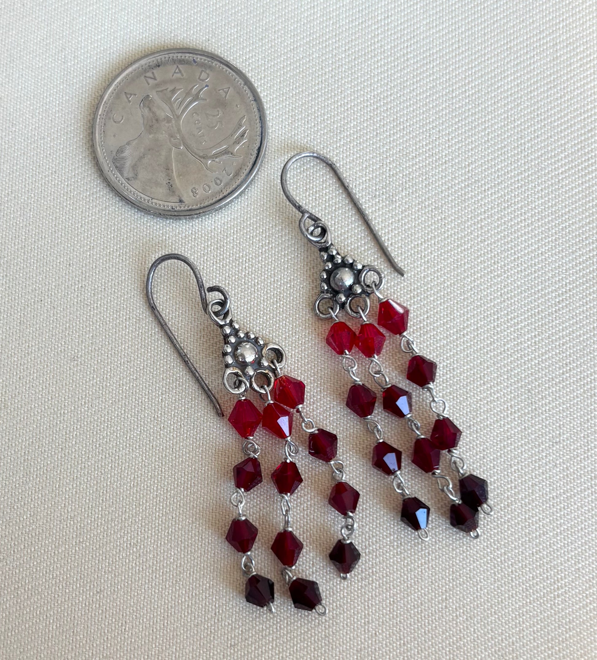 Pair of red beaded earrings with silver hooks on a light gray background, next to a quarter for scale.