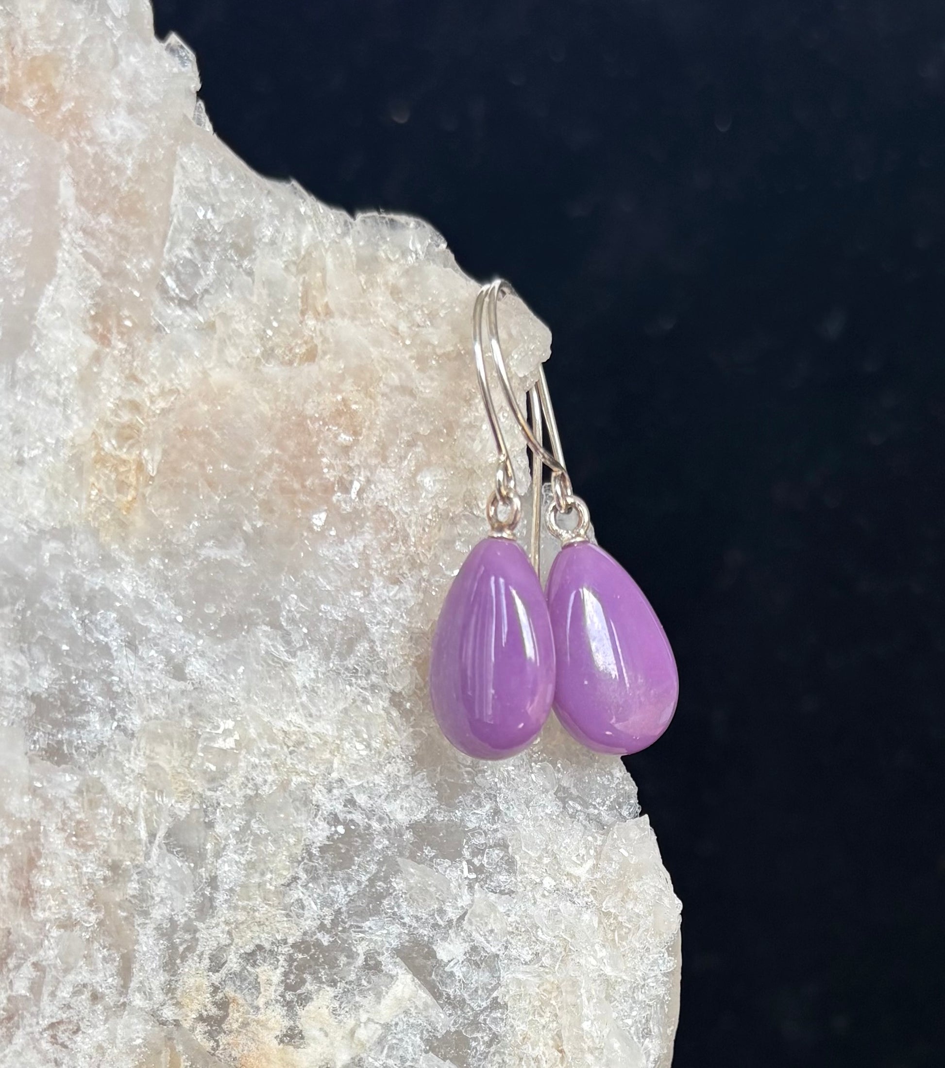 Purple teardrop earrings on a dark background with a textured surface