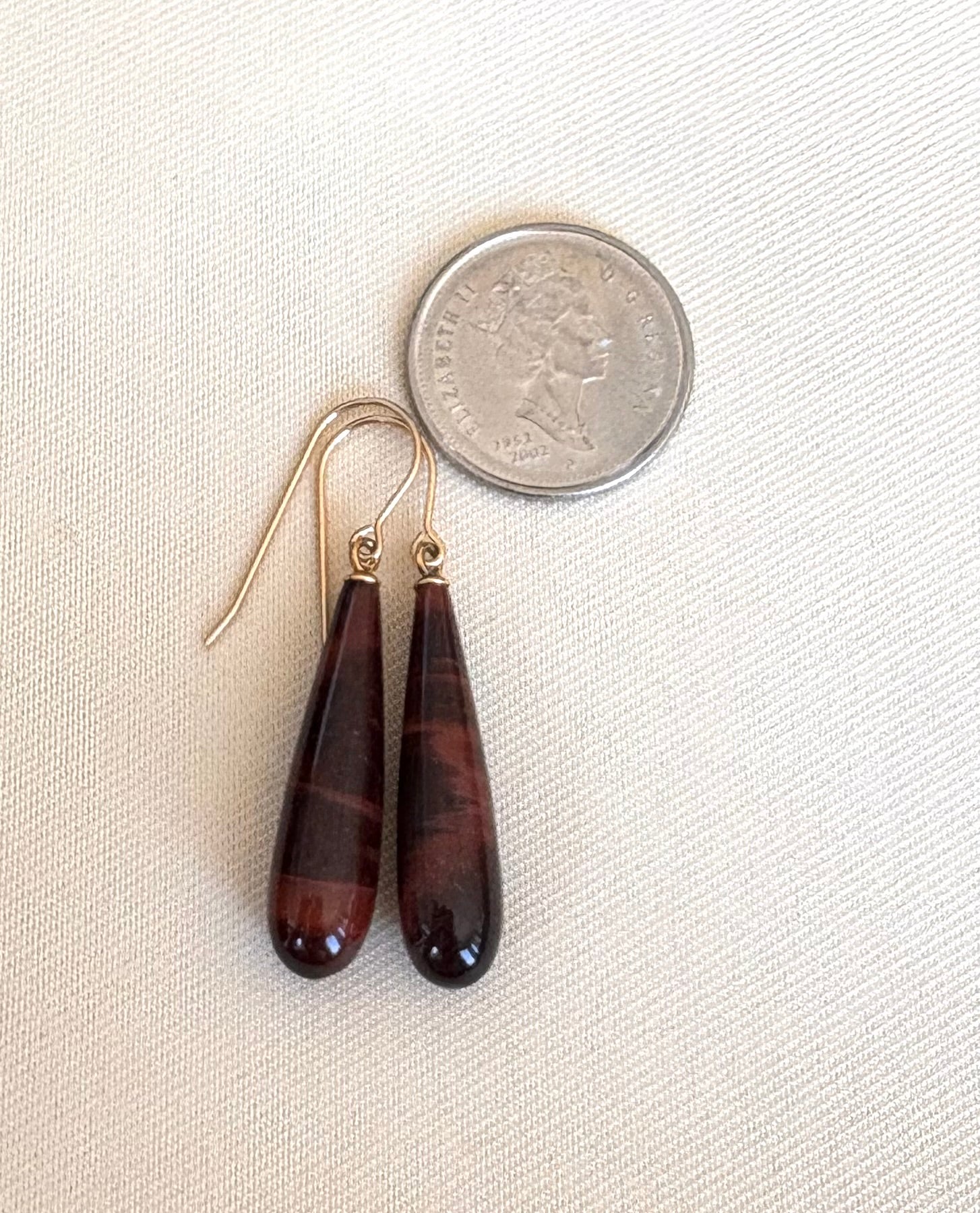 Brown teardrop earrings on a beige fabric background with a quarter for scale.