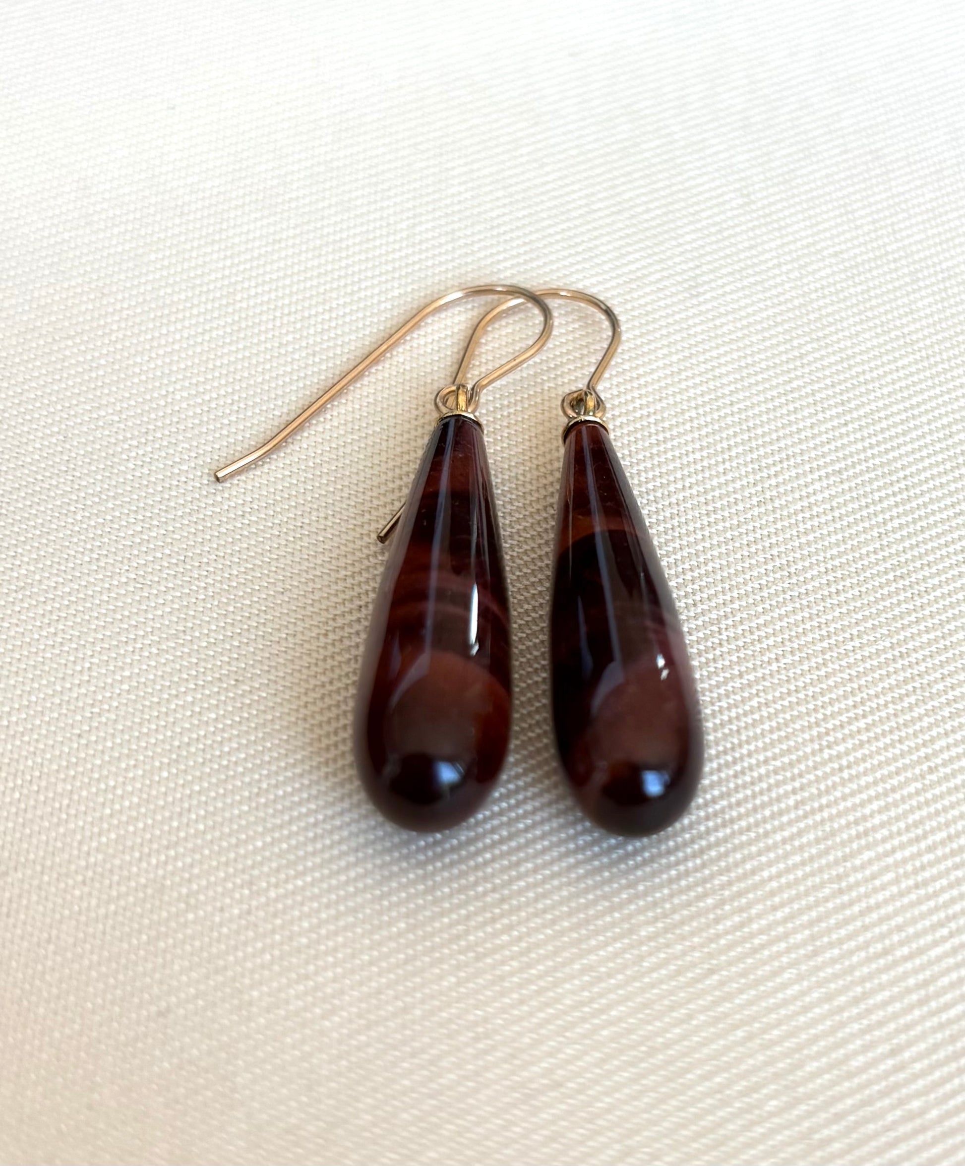 Teardrop-shaped Tiger's Eye  earrings on a beige fabric background