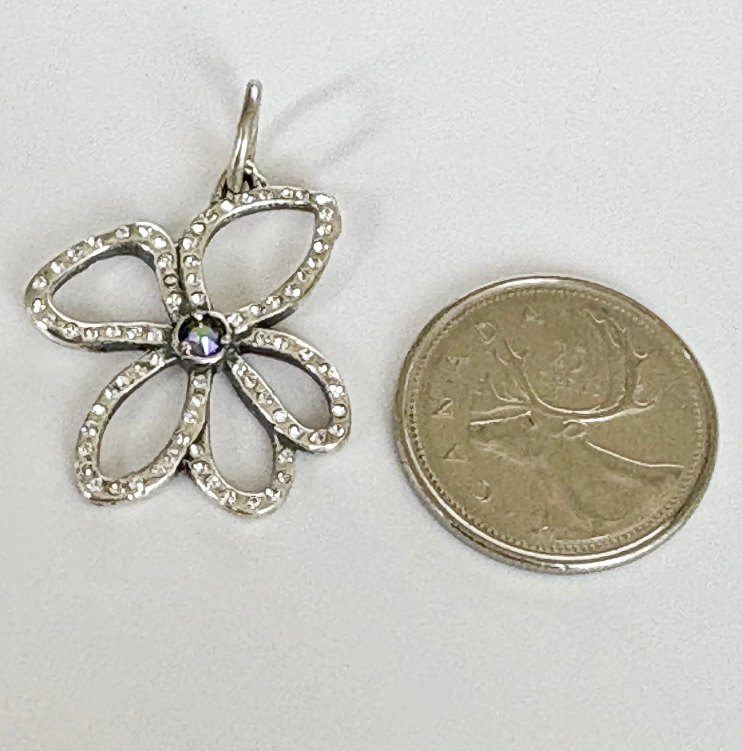 Sterling Silver flower-shaped pendant next to a coin on a white background