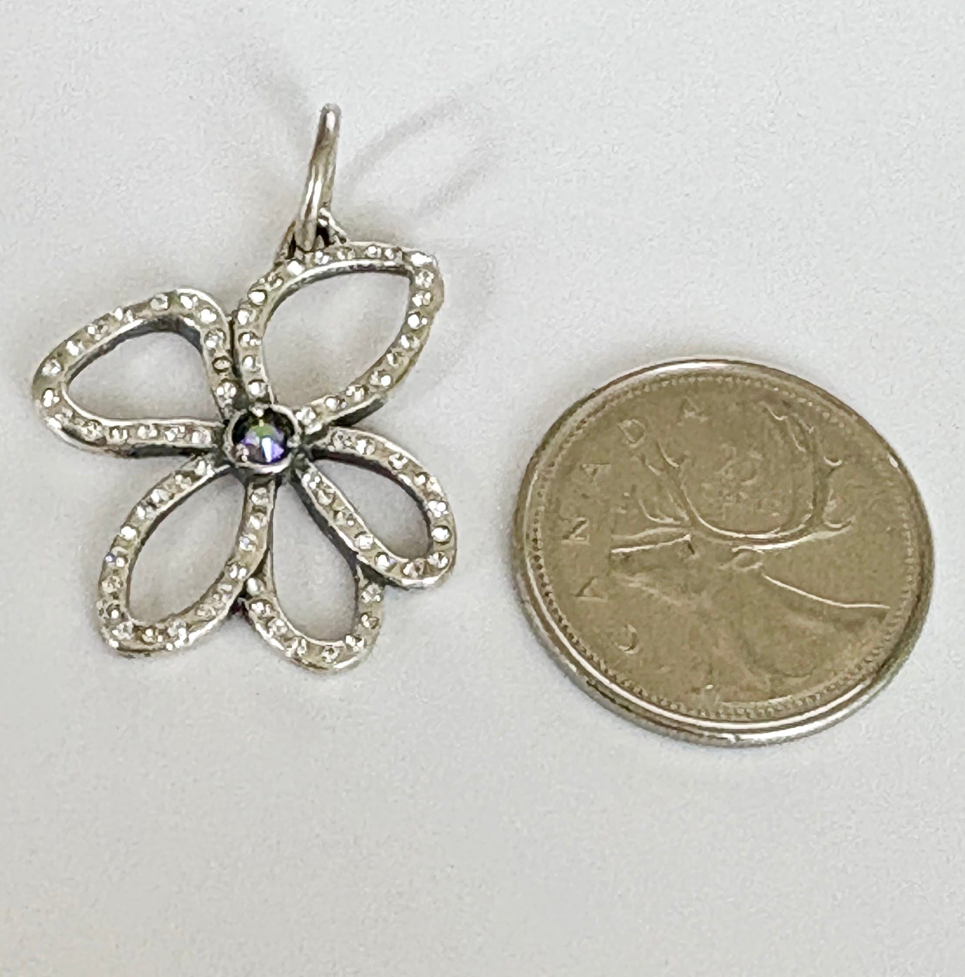 Sterling Silver flower-shaped pendant next to a coin on a white background