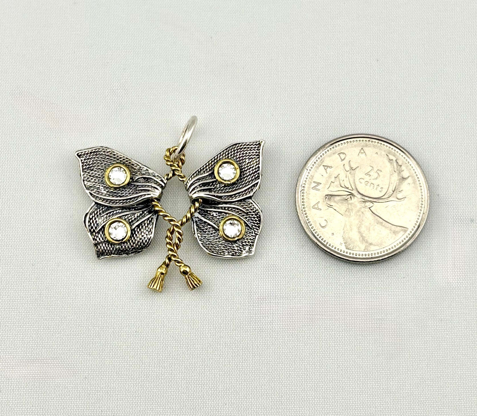 Butterfly-shaped pendant with gemstones next to a Canadian quarter coin on a light gray background