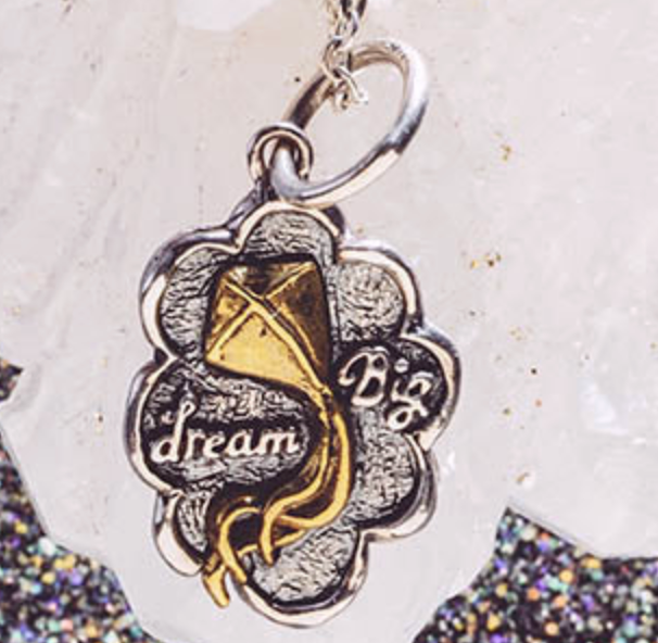 Silver and gold pendant with 'dream' text on a textured surface