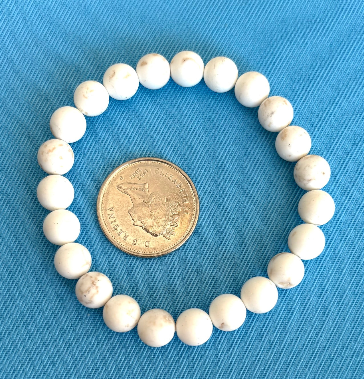 White beaded bracelet with a coin for size comparison on a blue background