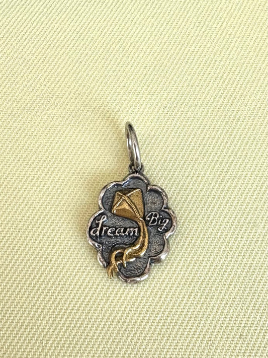 Waxing Poetic silver and gold pendant with 'dream Big' text on a beige fabric background